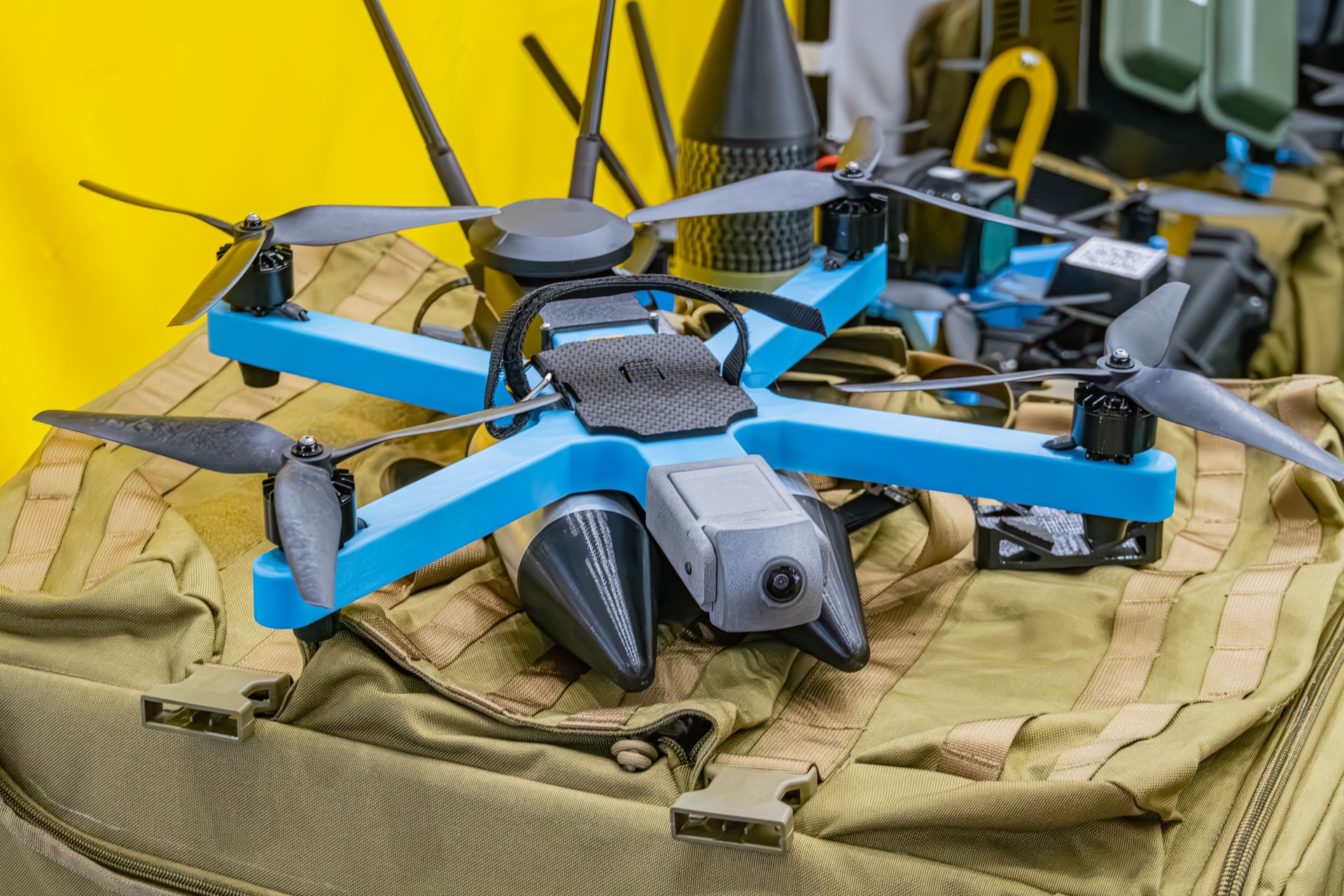 DJI Mavic Pro drone on green fabric surface amidst military equipment, indoor environment, foldable arms and propellers black silver, perspective from above